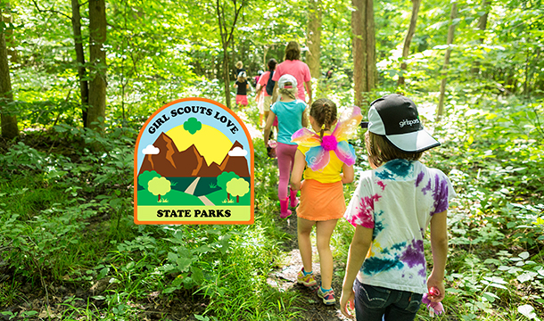 two young girl scouts outside at state park using binoculars - older girl is helping daisy girl scout see nature